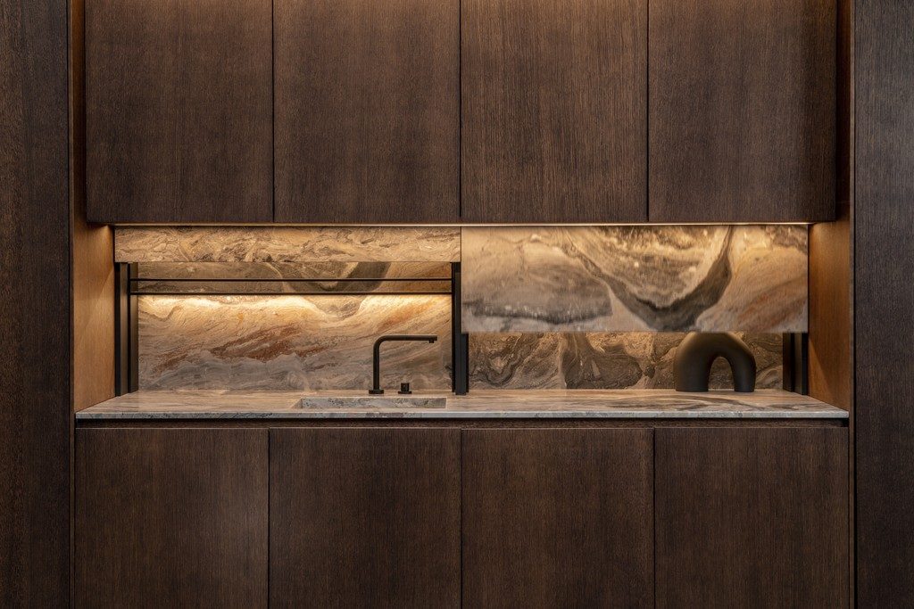 Wood-panelled kitchen cabinetry with a marble waterfall island, designed by colorlab.